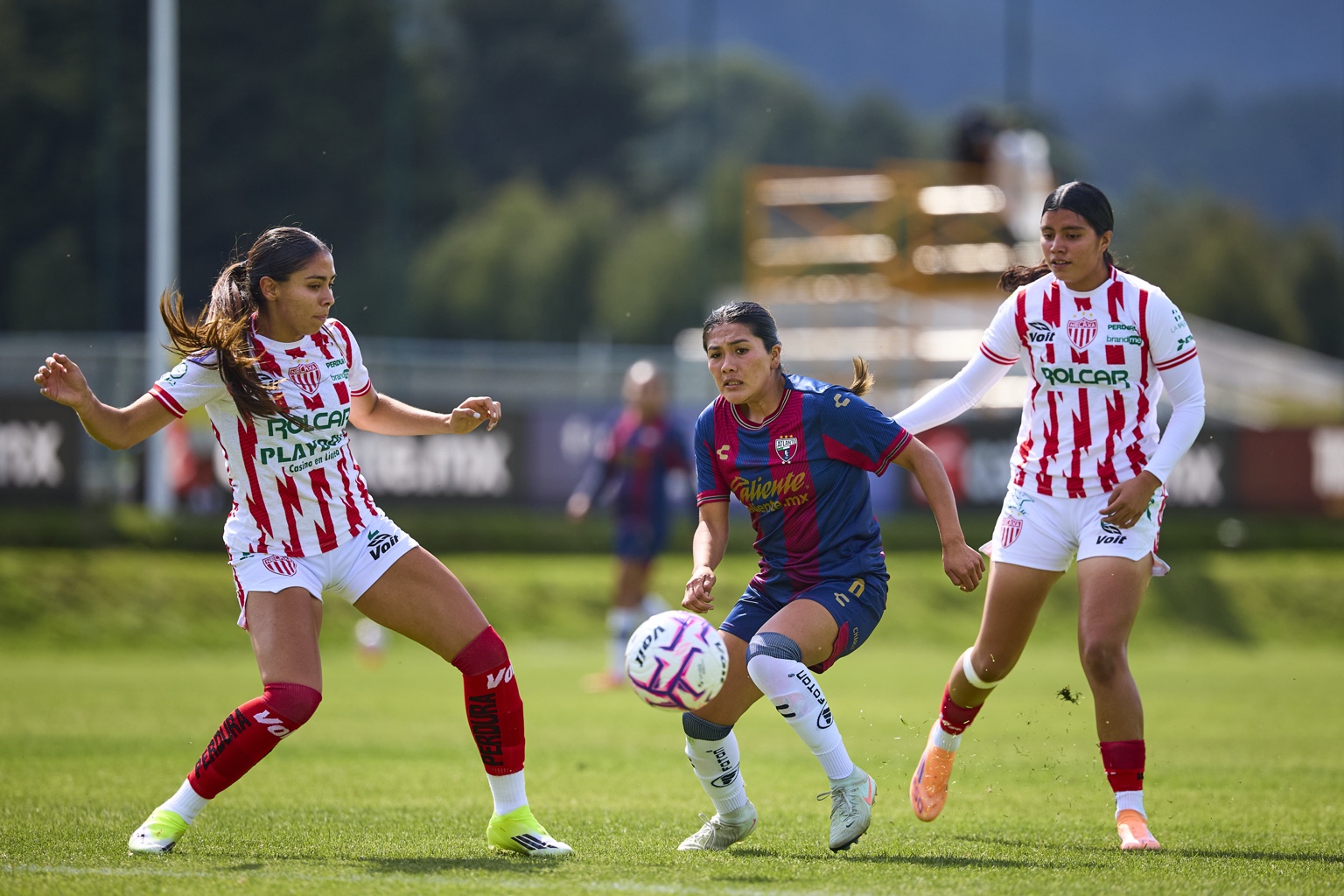 Una futbolista de Atlante conduce el balón entre dos rivales de Necaxa